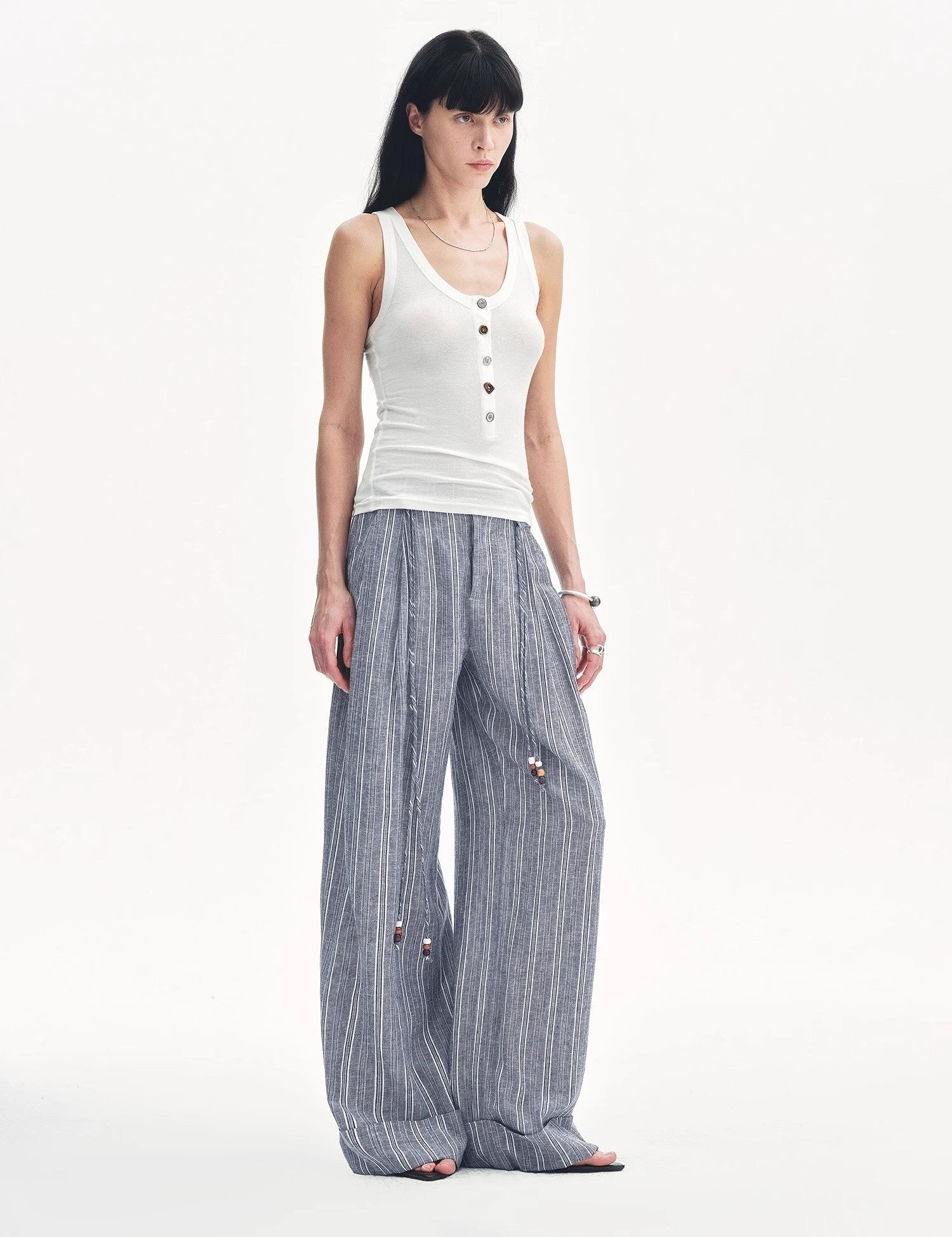 Woman wearing a white Lureva U-Henley vest and wide-legged striped pants, showcasing minimalist style for a breathable, chic look.