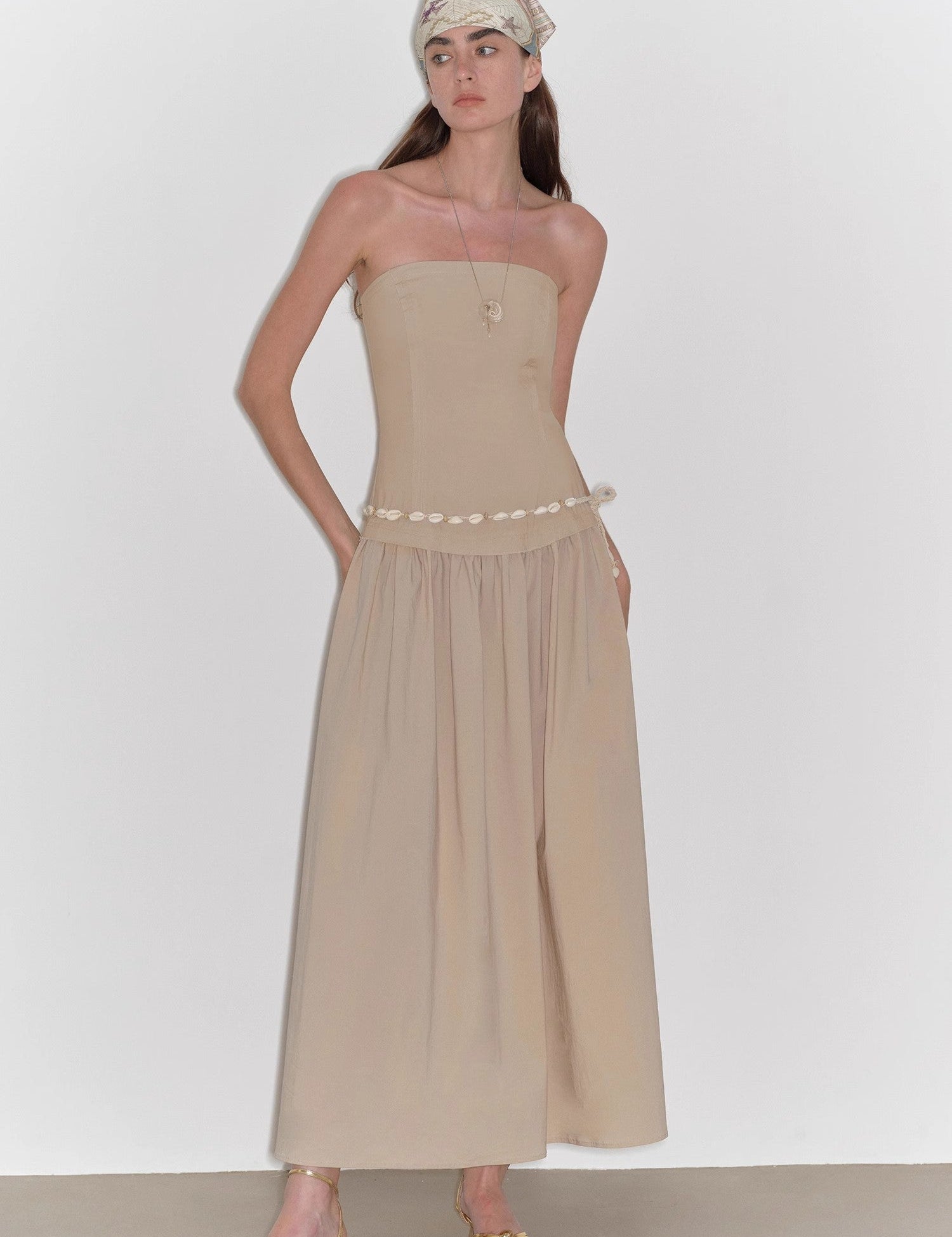 Woman wearing Aveline Bustier A-Line Dress in beige, showcasing strapless style with A-line skirt for vintage poise and summer elegance.
