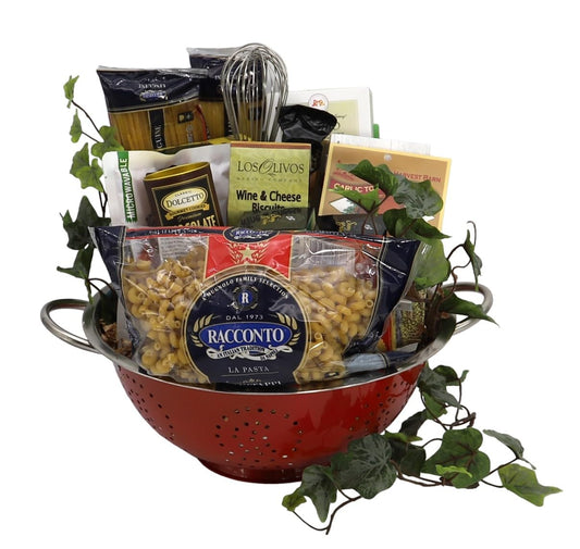 Italian Holiday Feast Gift Basket with pasta, sauce, biscotti, wine biscuits, and more in a red colander, decorated with greenery.