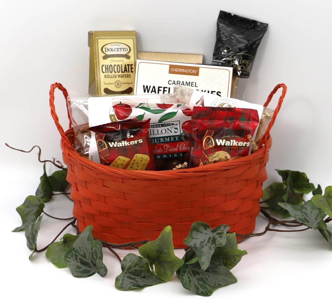 Gourmet gift basket with sausages, cheeses, nuts, and snacks in a red woven basket, surrounded by green ivy. Perfect for gifting.