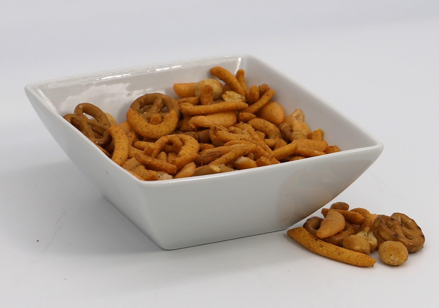 White bowl filled with gourmet snack mix including pretzels and nuts.