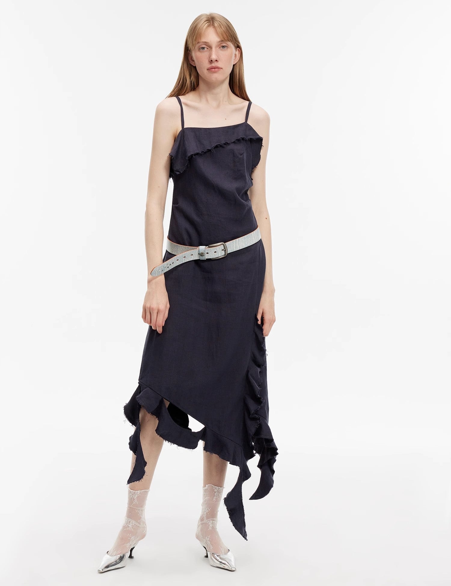 Woman wearing Elanys sand-washed linen ruffle dress with asymmetric neckline and pleated waist, highlighting summer's effortless romance.