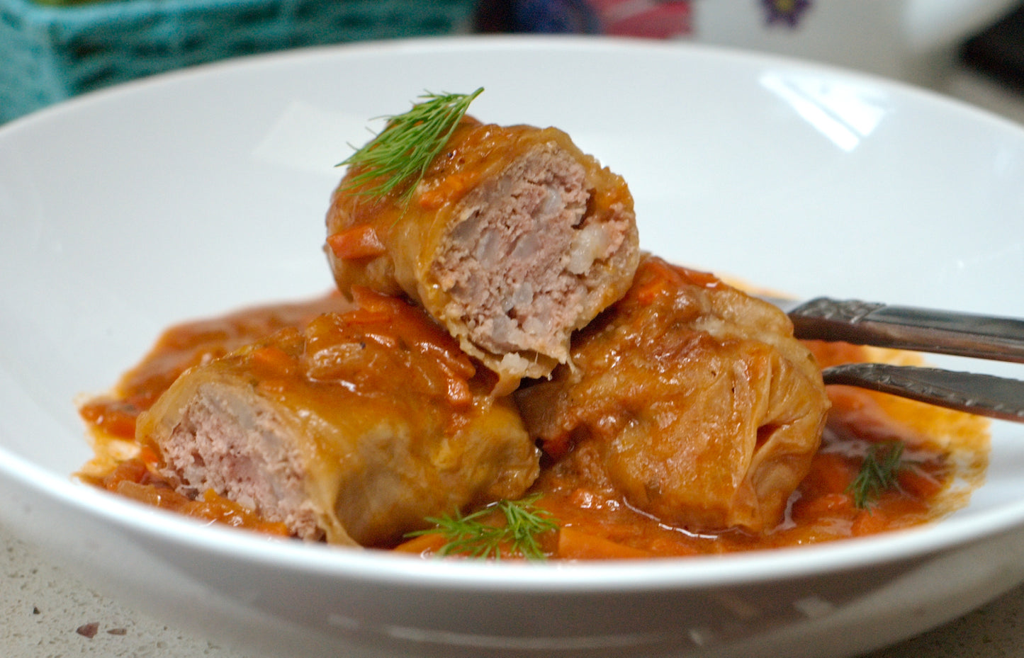 Homemade Ukrainian Holubtsi stuffed cabbage rolls with meat and rice, served in tomato sauce on a white plate.