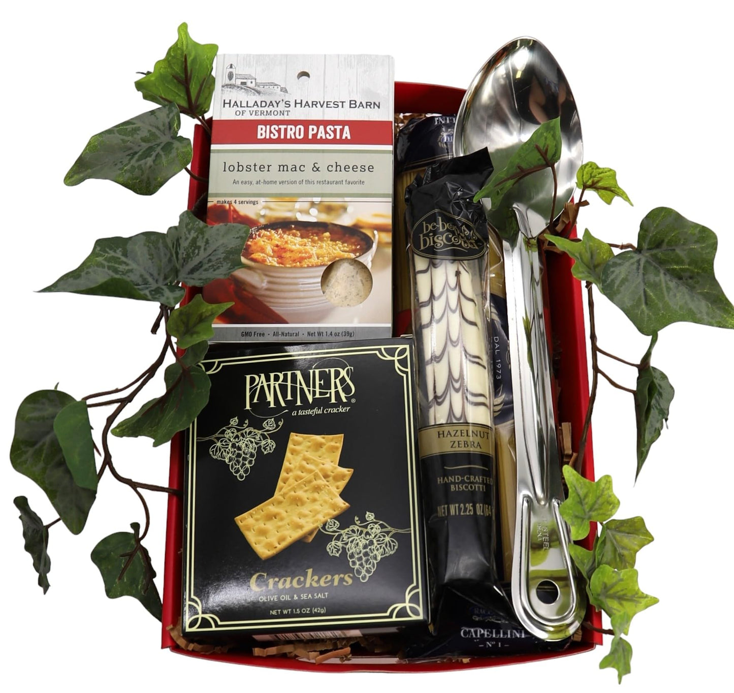 Gourmet Italian gift tray with pasta, biscotti, crackers, and utensils surrounded by green leaves.