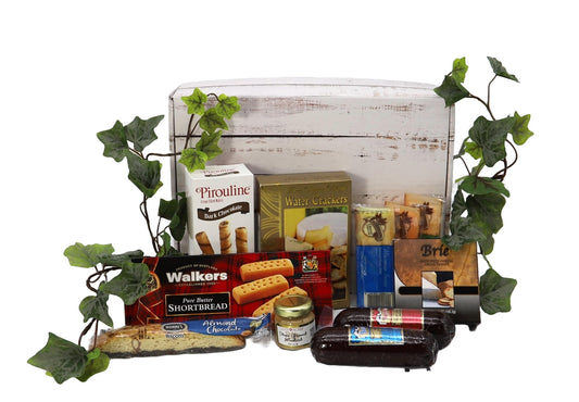 Trail Adventure Snack Box with sausages, cheeses, crackers, sweet treats, ideal for picnics, hikes, and road trips, surrounded by greenery.