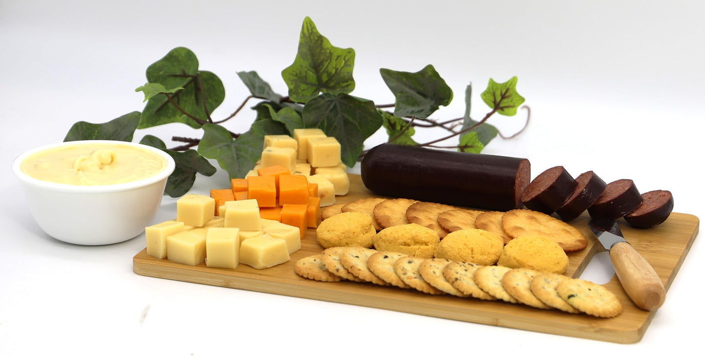 Trail adventure snack box with sausages, cheeses, crackers, and sweet treats on a serving board with greenery in the background.