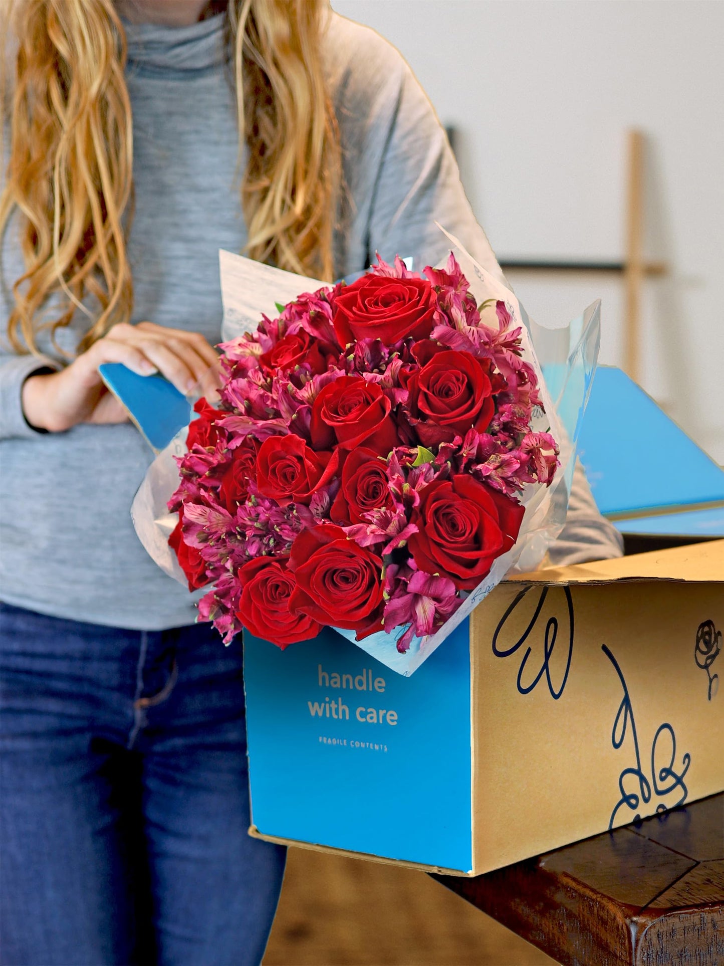 Bouquet of red roses and alstroemeria being unboxed by a woman, showing vibrant fresh blooms and sustainable packaging.