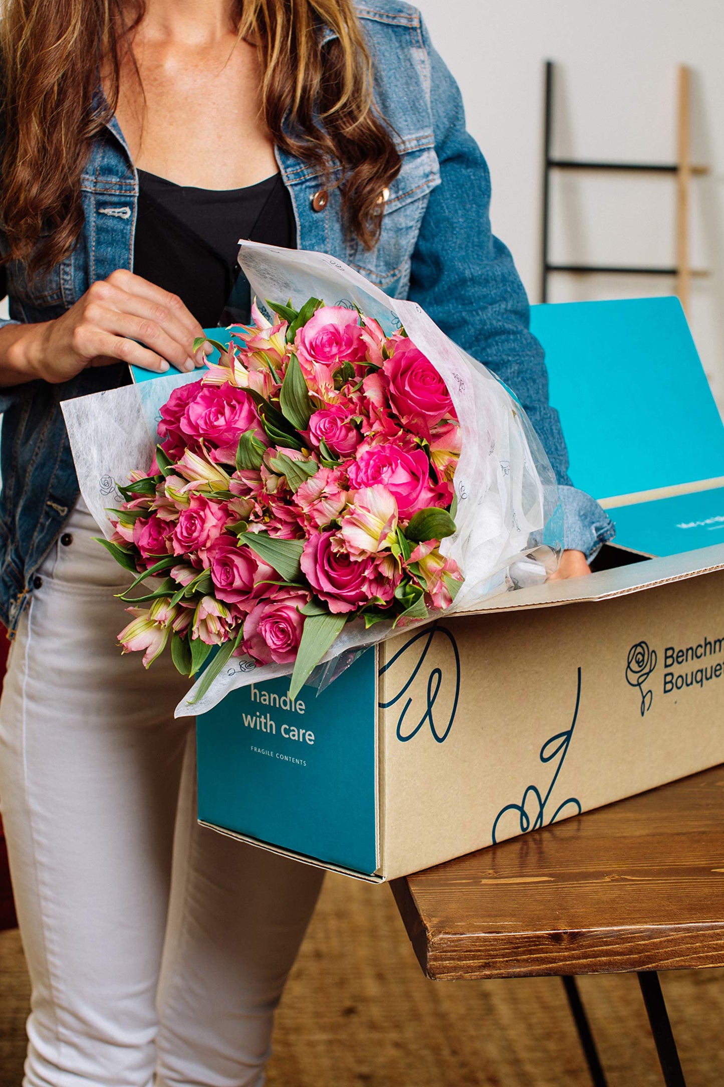 Woman unpacking vibrant bouquet of pink roses and alstroemeria from box, perfect for special occasions and sourced sustainably.