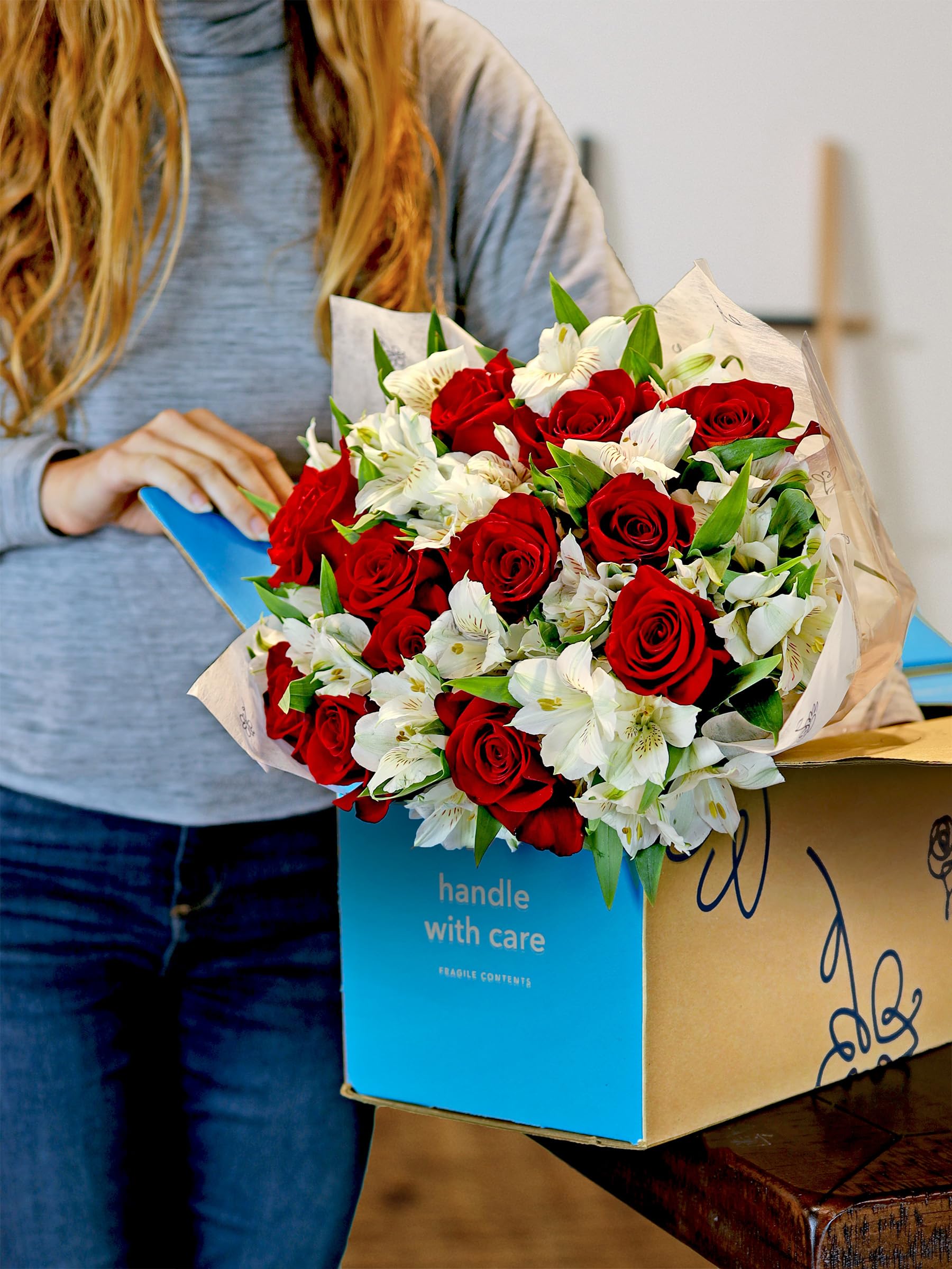 Woman opening box of fresh red roses and white alstroemeria bouquet, handle with care.