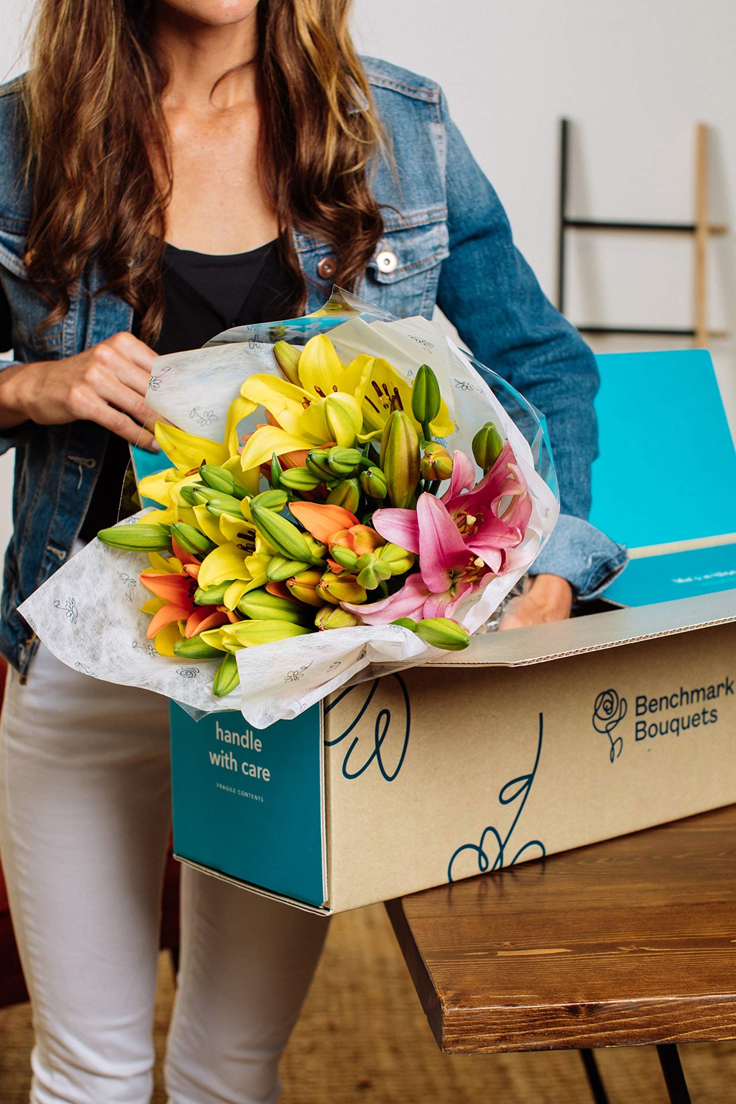 Woman holding 12-stem Asiatic lilies bouquet with vibrant blooms from Benchmark Bouquets, packaged in a gift box.