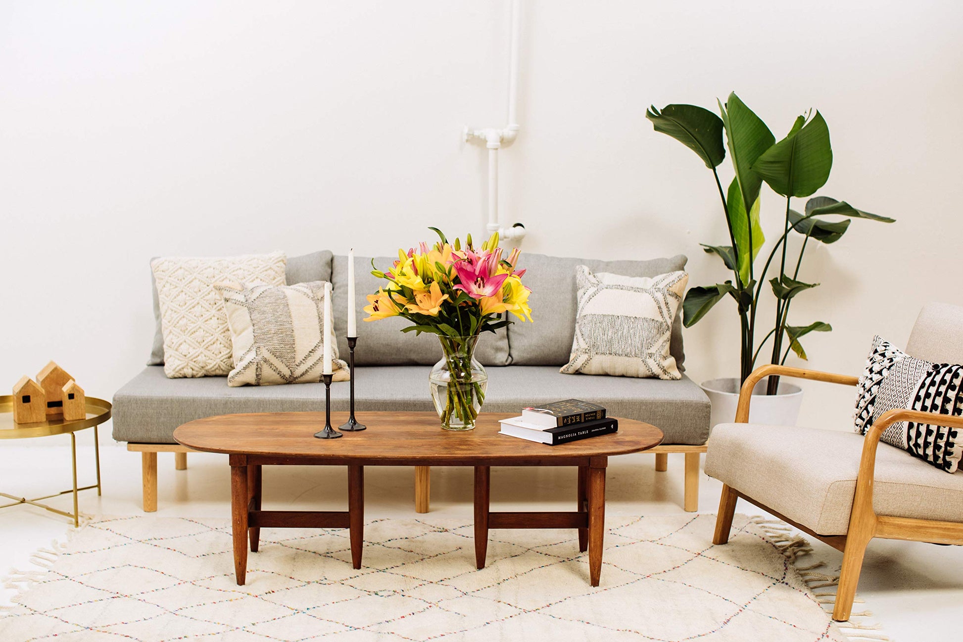 Bouquet of 12 Asiatic lilies in a glass vase on a stylish wooden coffee table in a modern living room setting.