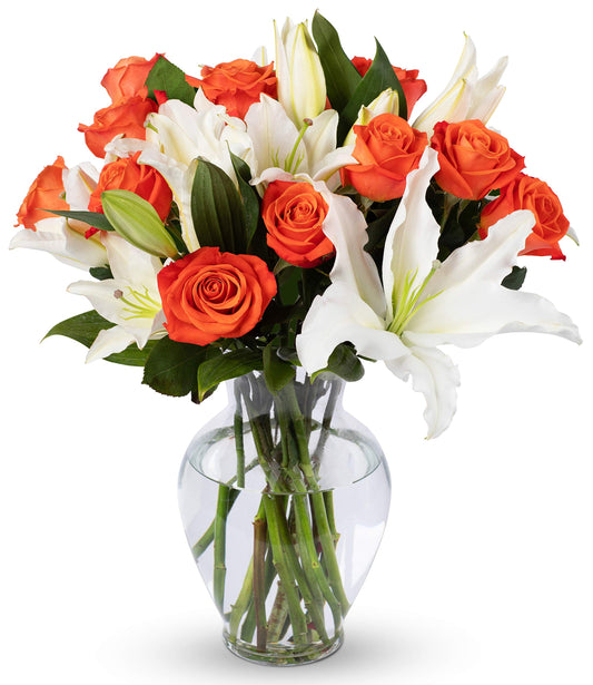 Elegant bouquet of orange roses and white lilies in a glass vase, symbolizing beauty and sustainability for special occasions.