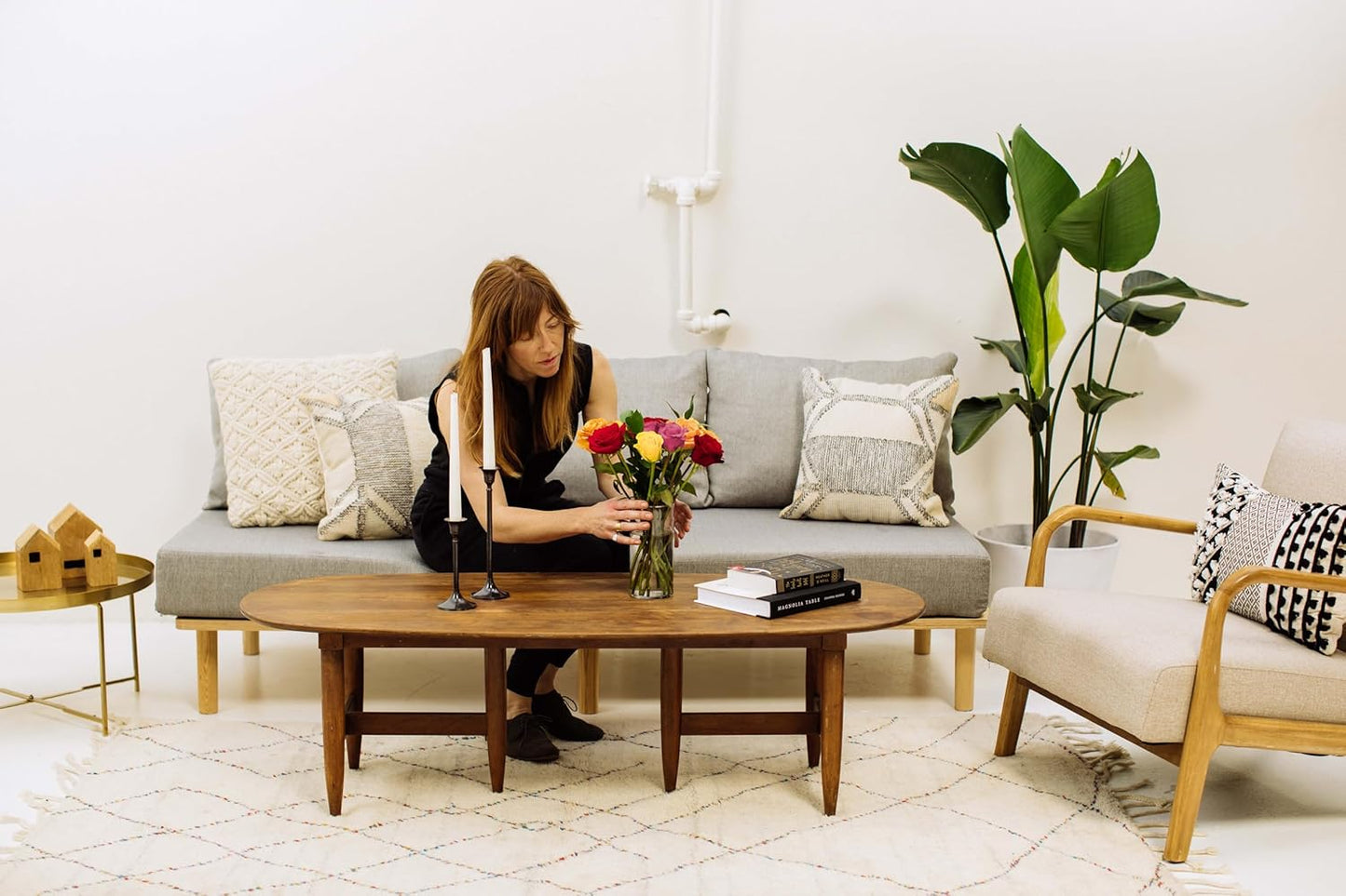 Woman arranging vibrant flower bouquet in modern living room setting with wooden furniture and stylish decor.