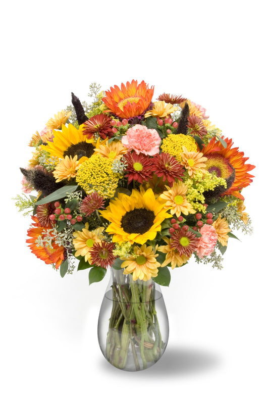 Vibrant autumn bouquet with sunflowers and eucalyptus in a clear vase, showcasing seasonal fall flowers and rich colors.