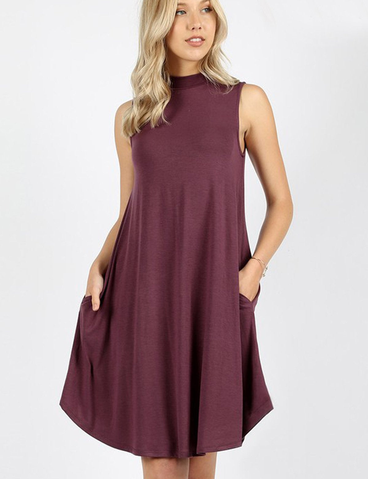Woman wearing Urban Muse Mock Neck Dress in eggplant color with side pockets, showcasing modern, sleeveless design and knee-length hem.