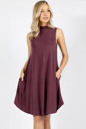 Woman wearing Urban Muse Mock Neck Dress in eggplant color with side pockets, showcasing modern, sleeveless design and knee-length hem.