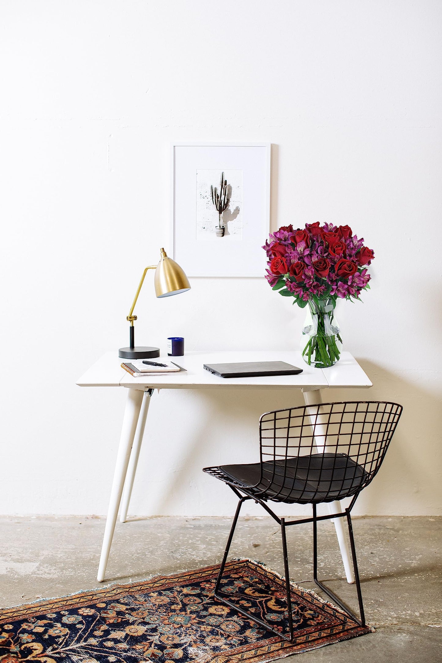 Modern workspace with pink roses and alstroemeria bouquet in a glass vase on a white desk.