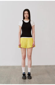 Model wearing Isvera Slim Cotton Camisole in black, paired with yellow shorts and white socks on a plain background.