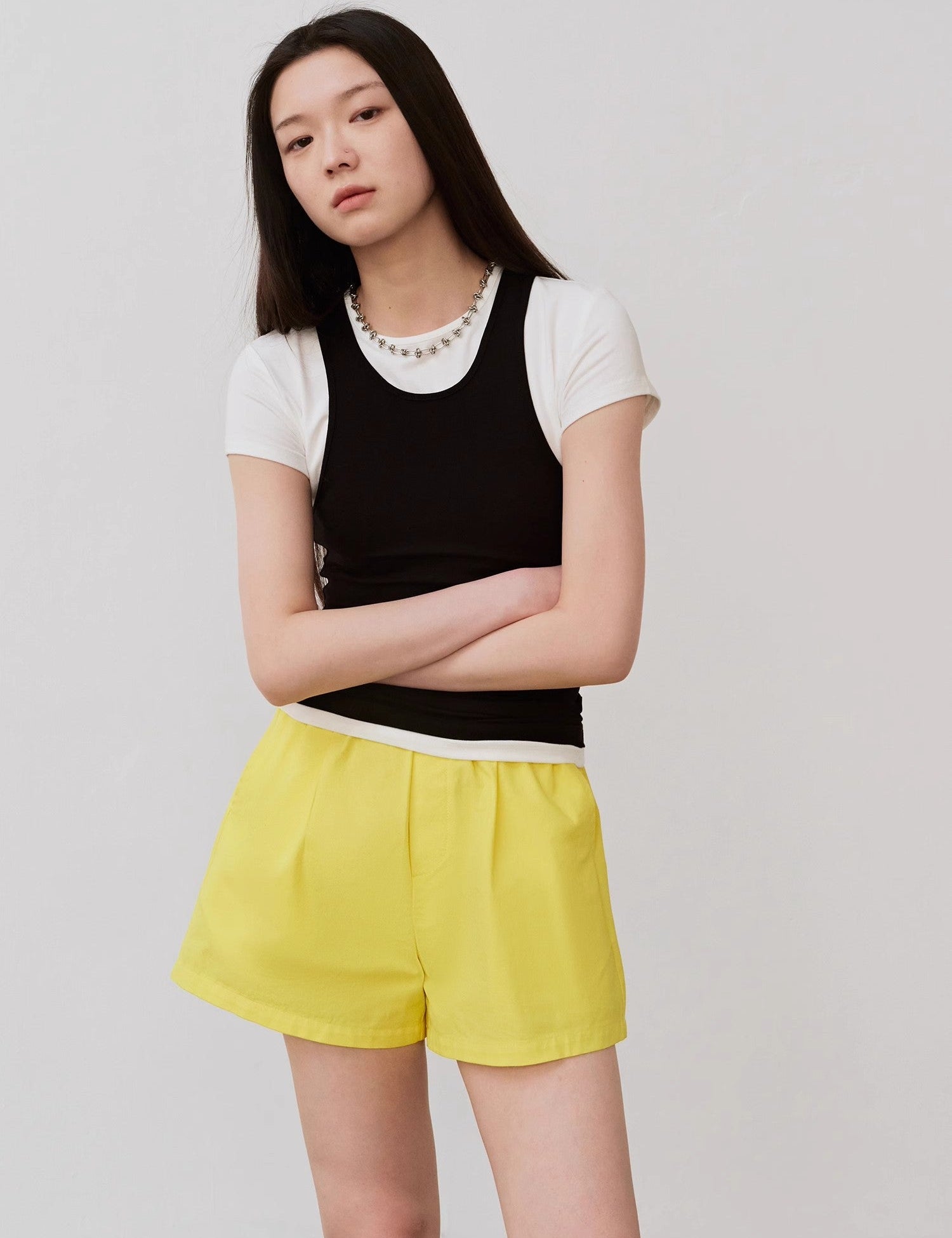 Woman wearing black camisole and yellow shorts, posing against a neutral background.