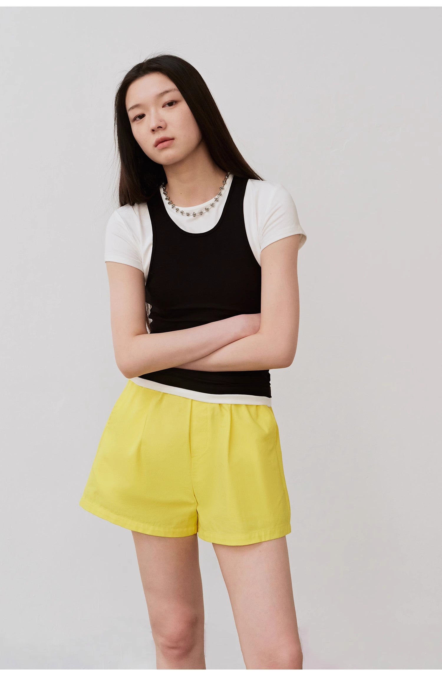 Woman wearing black camisole and yellow shorts, posing against a neutral background.