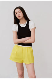 Woman wearing black camisole and yellow shorts, posing against a neutral background.