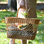Hand carrying a rattan-style picnic basket on grass, perfect for picnics, shopping, or home decor, showcasing its handmade woven texture.