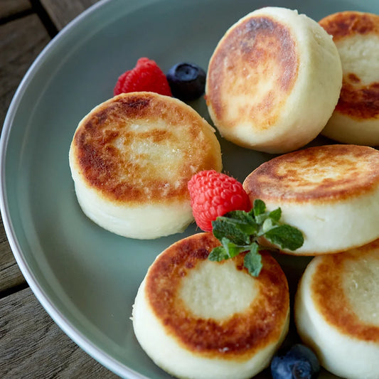 Plate of homemade Ukrainian syrnyky cheese pancakes with fresh berries, lightly pan-fried to golden perfection.