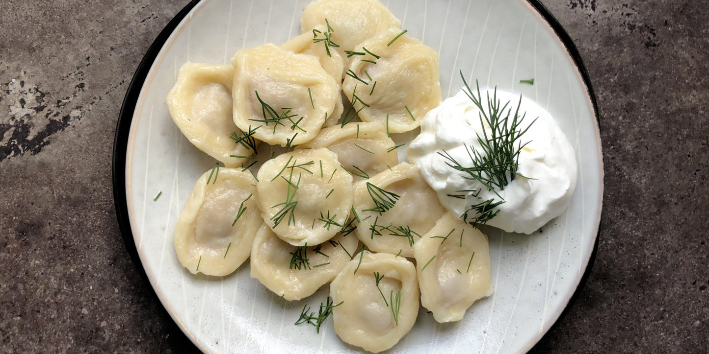 Plate of homemade Ukrainian pelmeni dumplings with fresh dill and a side of sour cream.