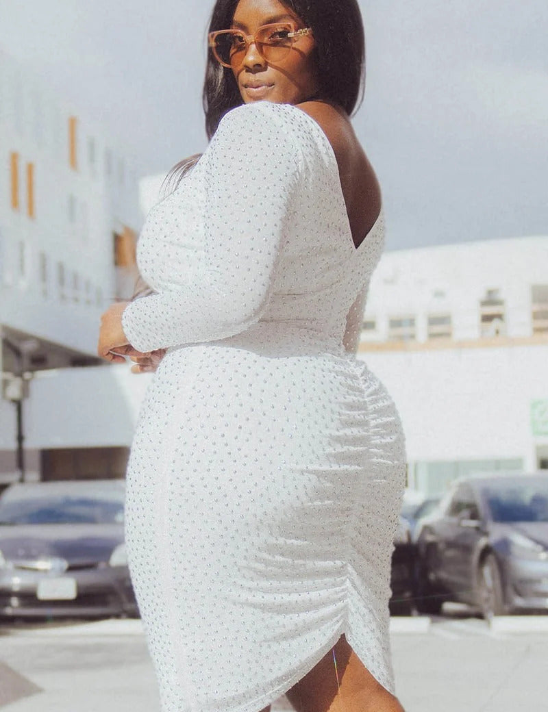 Woman wearing Isalyn Sparkle Midi Dress with rhinestone accents and V-shaped back, showcasing sheer long sleeves and fitted midi skirt.