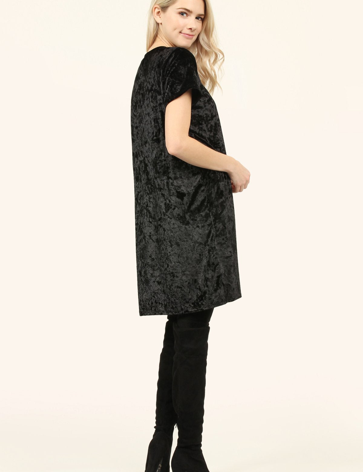 Woman wearing a black Calyn Crushed Velvet Tunic Dress with short sleeves and a crew neckline, styled with over-the-knee boots.