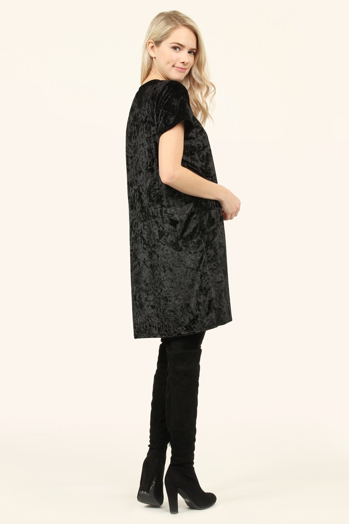 Woman wearing a black Calyn Crushed Velvet Tunic Dress with short sleeves and a crew neckline, styled with over-the-knee boots.