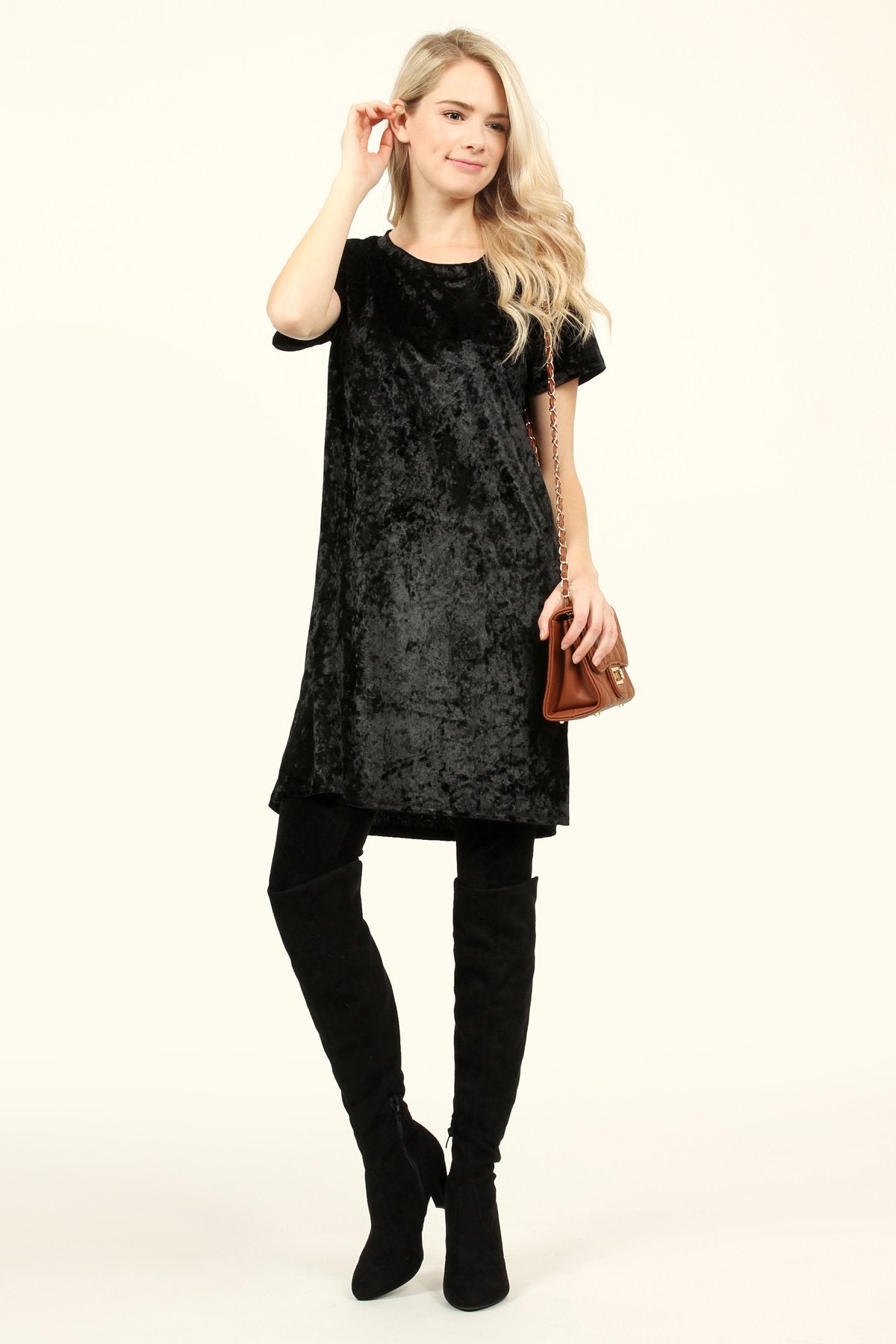 Woman wearing a black Calyn crushed velvet tunic dress with over-the-knee boots, showcasing a chic and versatile fashion look.