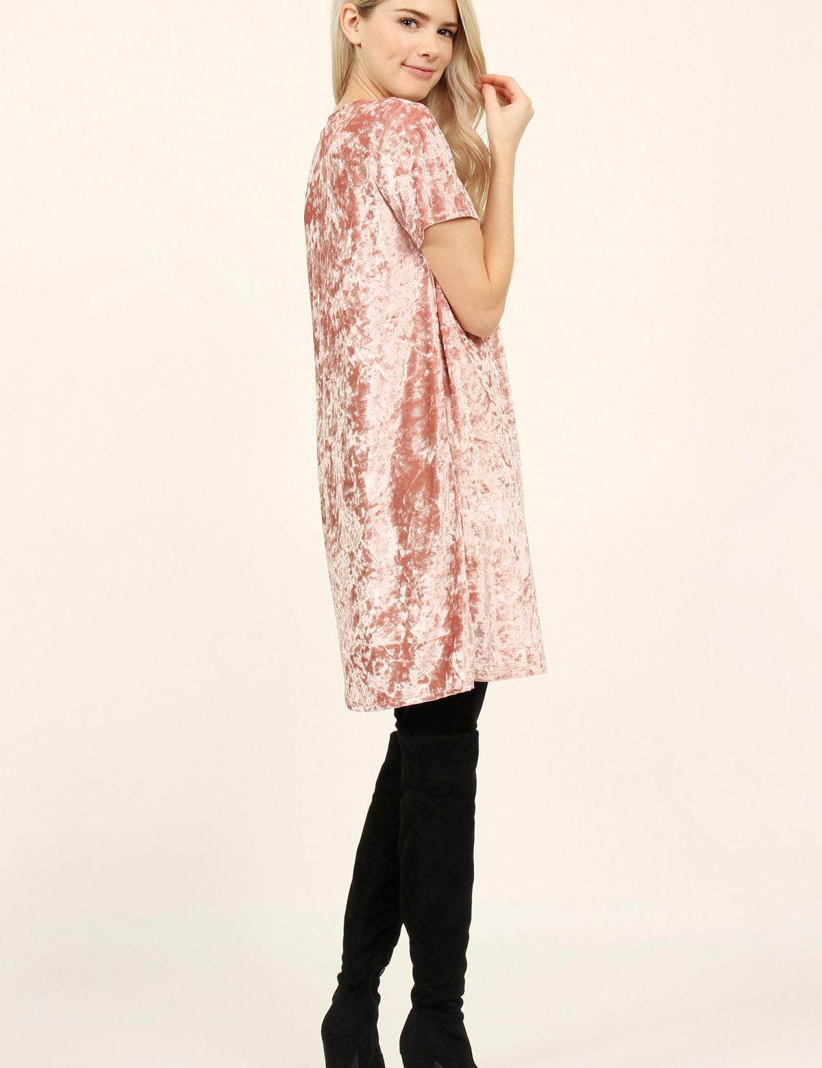 Woman wearing a pink Calyn Crushed Velvet Tunic Dress with black over-the-knee boots, showcasing the dress's soft texture and 32″ length.