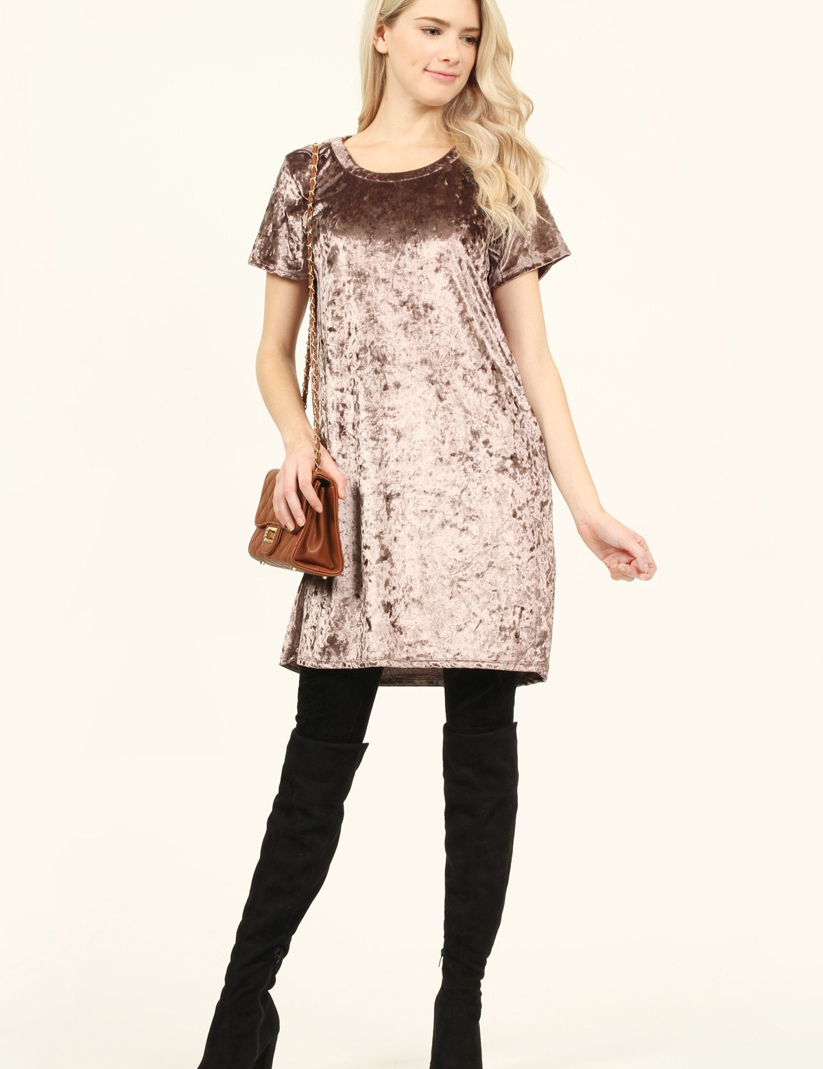 Woman wearing Calyn Crushed Velvet Tunic Dress in rose, paired with over-the-knee black boots and holding a brown leather purse.