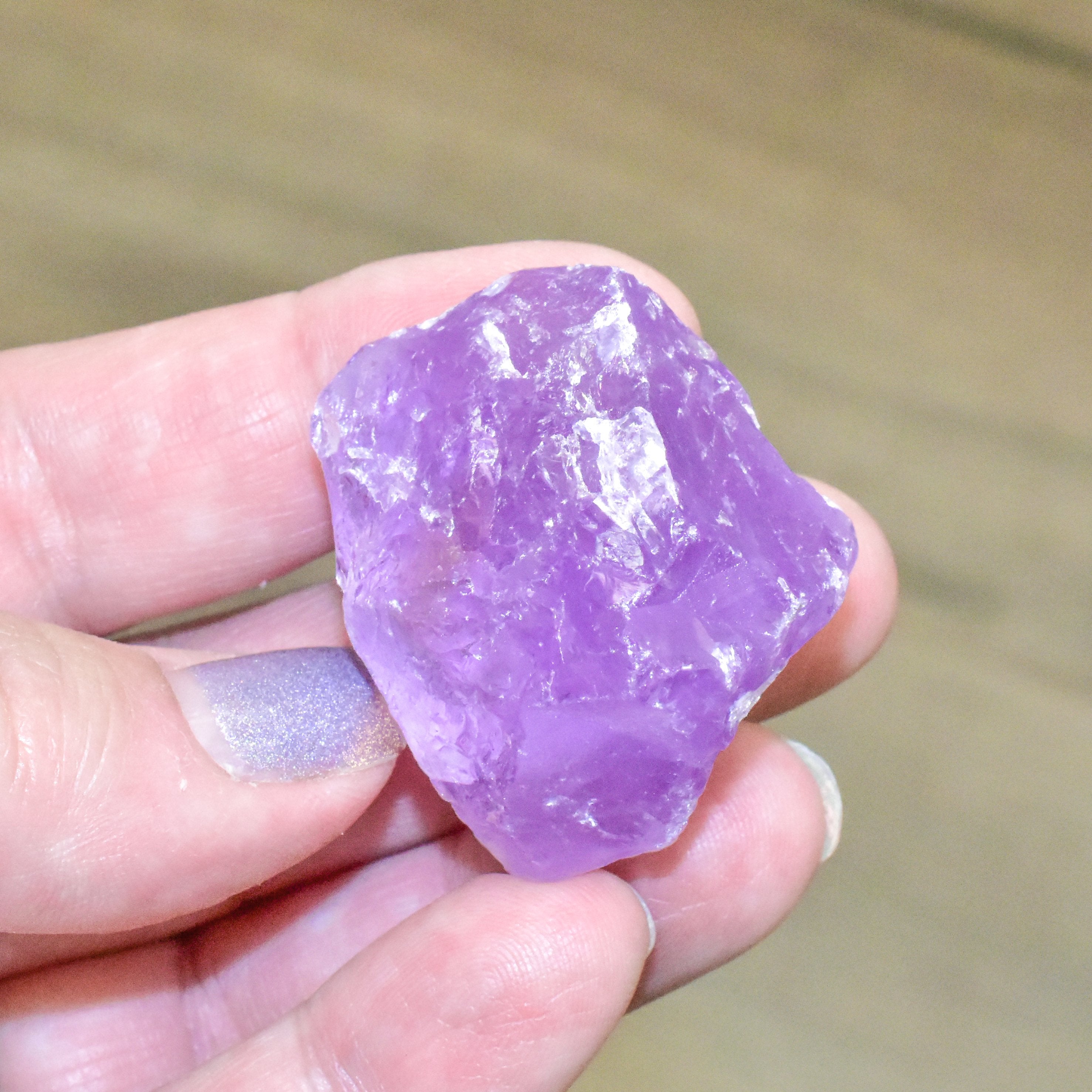 Hand holding a pocket-sized natural amethyst rough stone, known for calming energy and charged under super full moon.