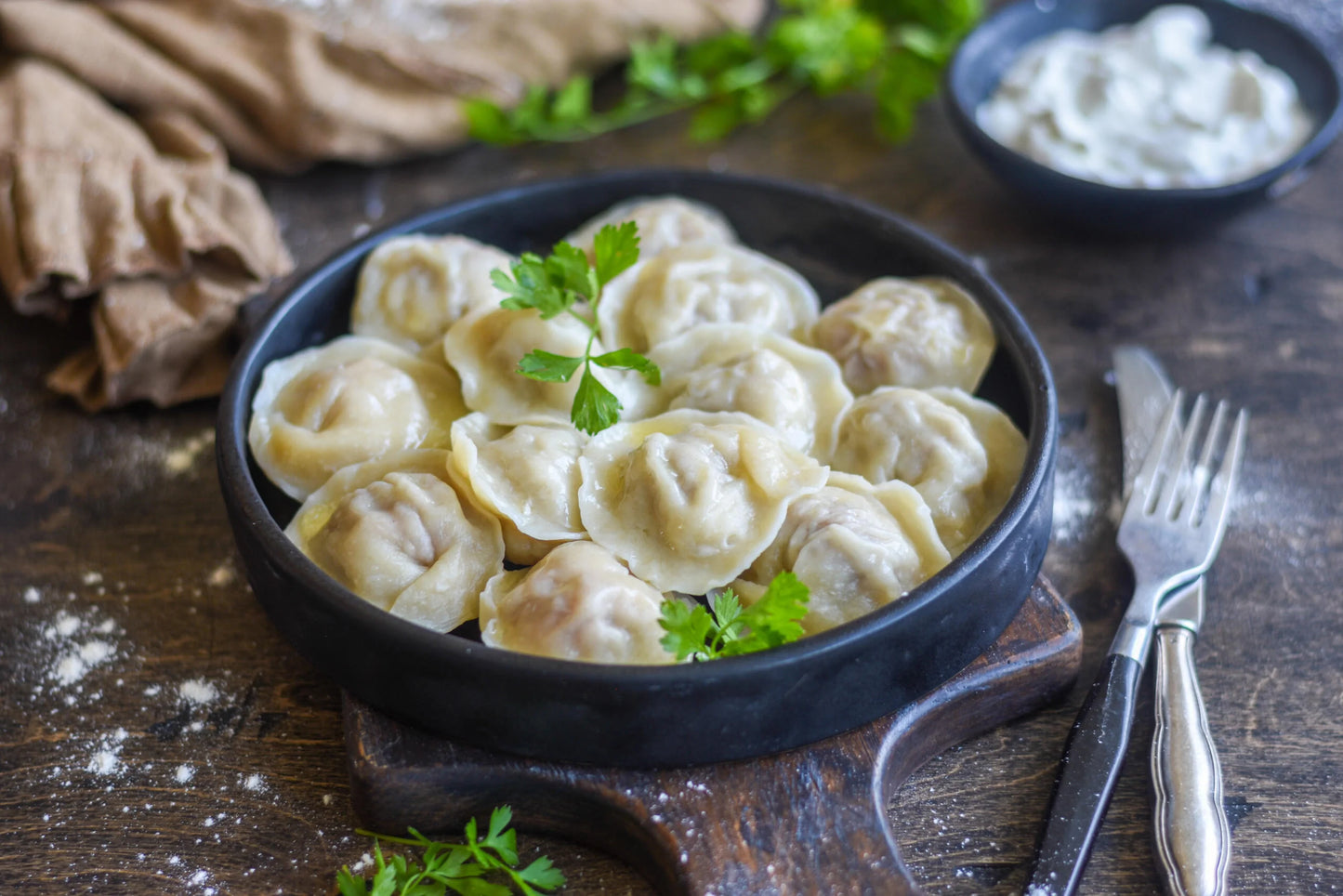 Plate of traditional homemade Ukrainian pelmeni dumplings displayed with fresh herbs on a wooden board