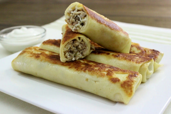 Golden-brown Ukrainian crepes filled with savory beef, served on a white plate, showcasing traditional homemade blini.