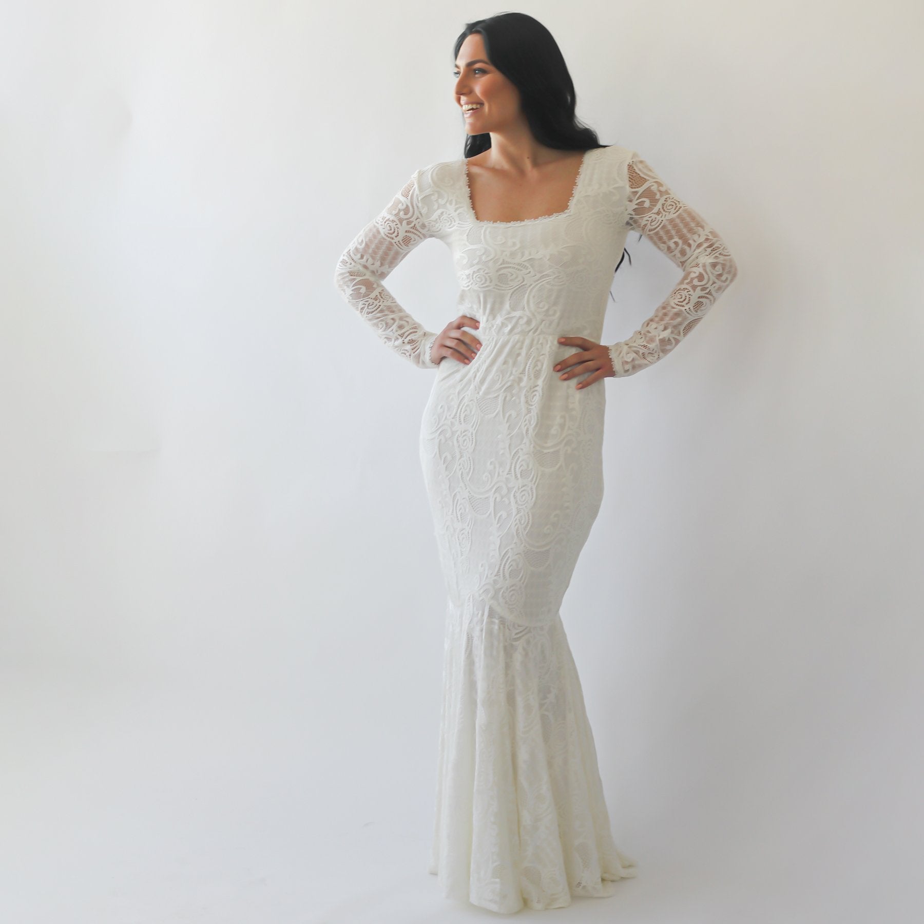Woman wearing Elirelle ivory lace mermaid wedding dress with long sleeves, square neckline, and fitted silhouette.