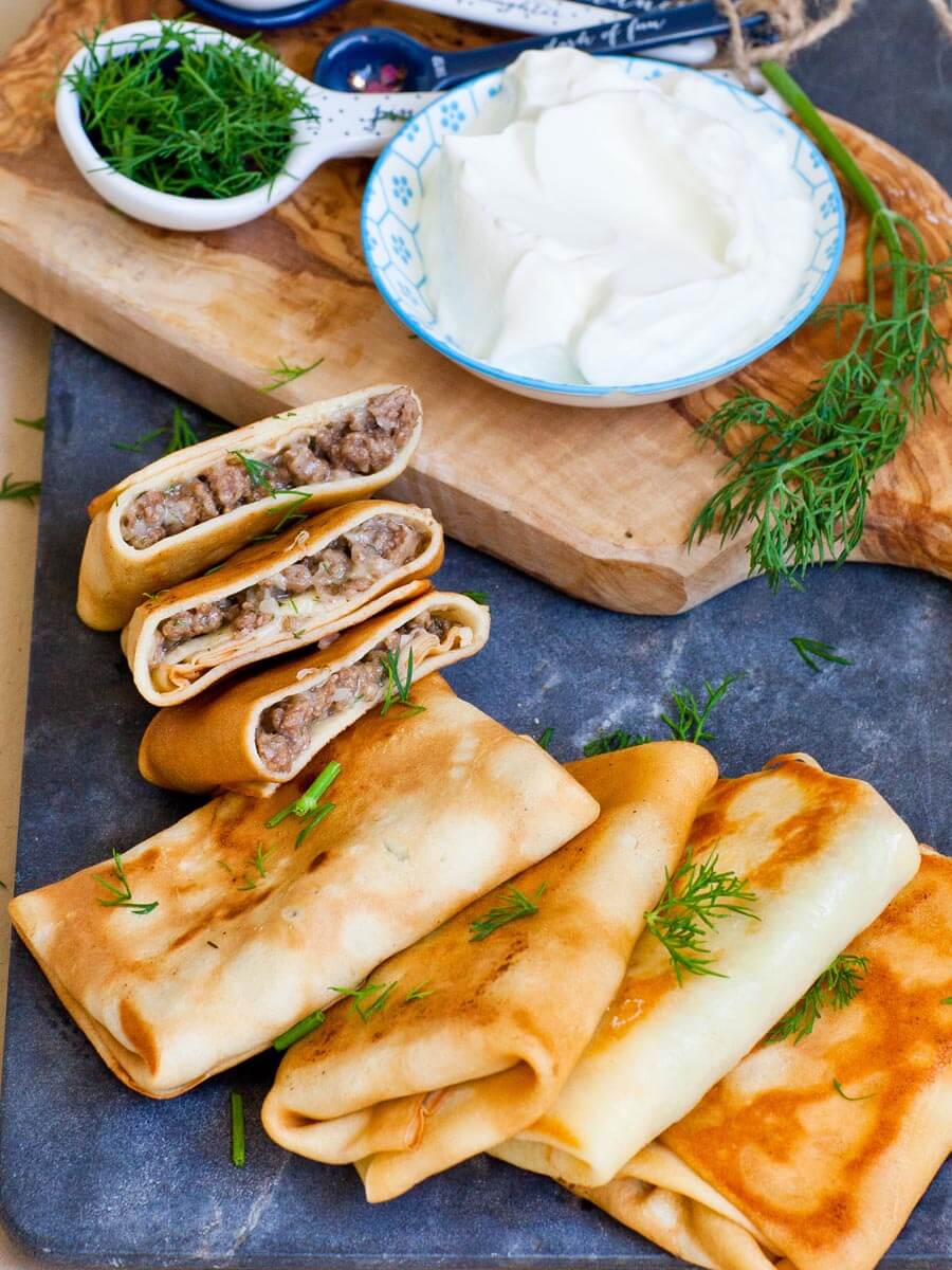 Homemade Ukrainian crepes with beef filling, garnished with fresh dill, served with a bowl of sour cream.