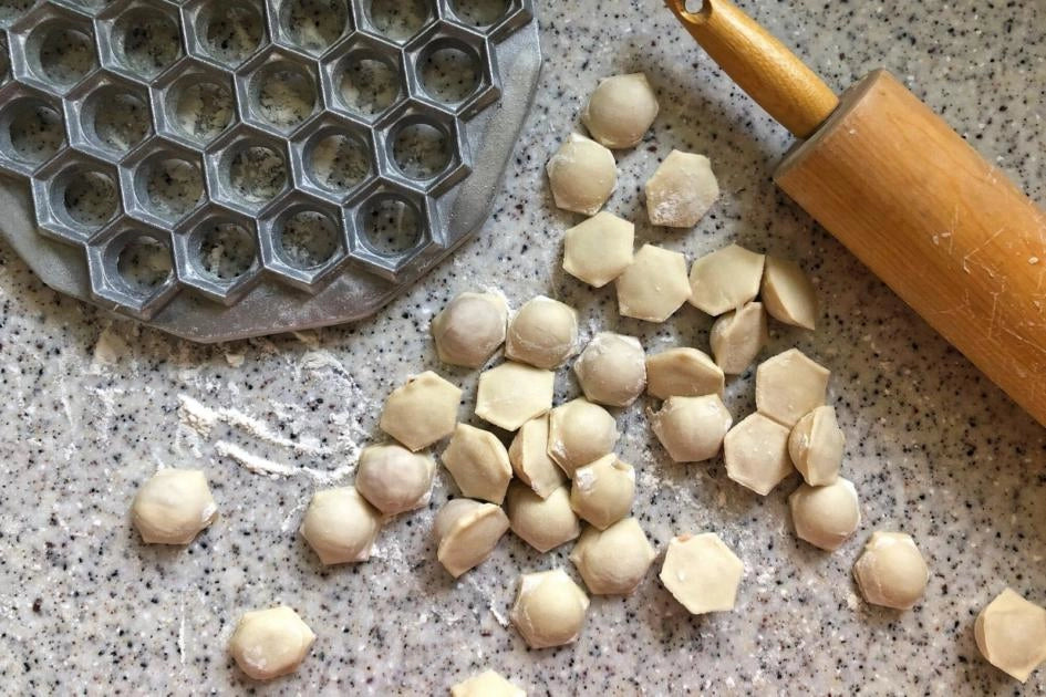 Homemade Ukrainian pelmeni dough and dumplings with rolling pin and mold on countertop.