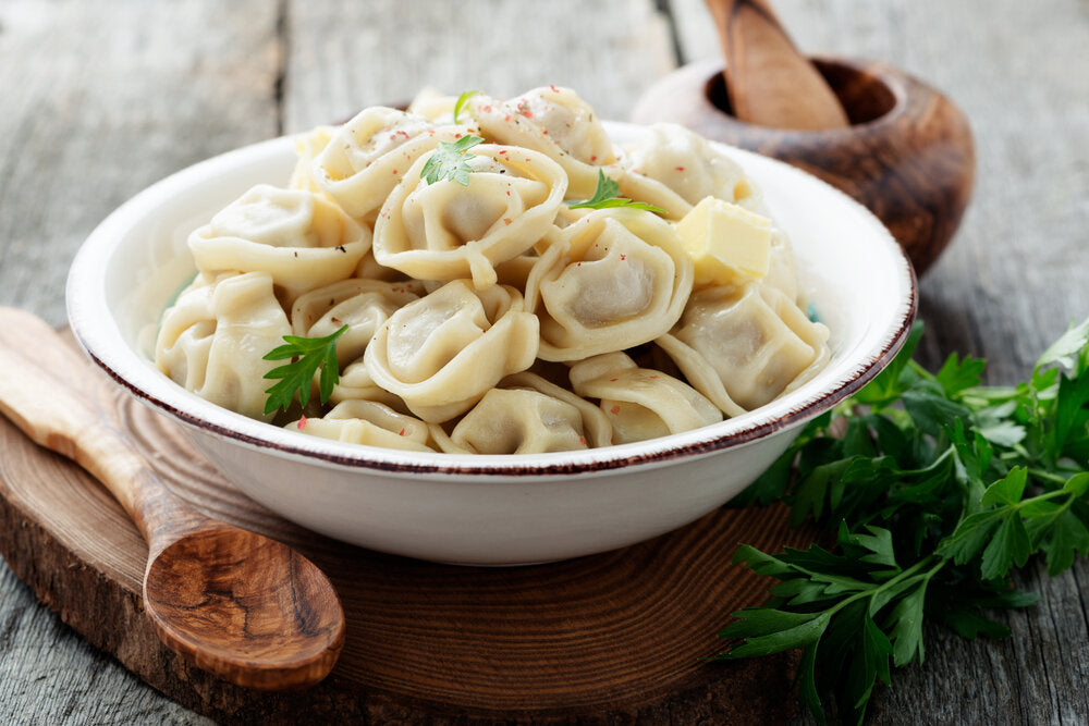 Bowl of traditional Ukrainian pelmeni dumplings on wooden table with fresh parsley garnish.