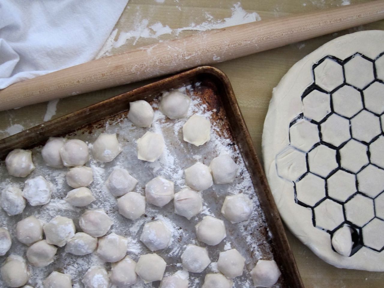 Homemade Ukrainian pelmeni dumplings on a tray with dough cutter, showcasing traditional preparation process.