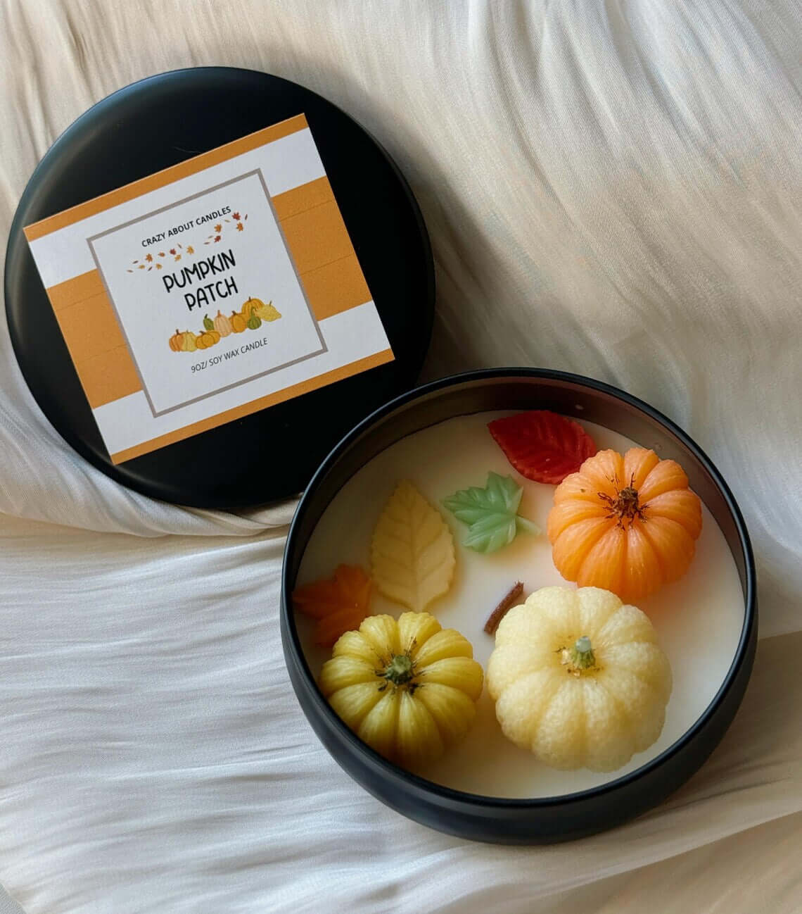 Soy wax candle in black tin adorned with pumpkin and leaf motifs, featuring autumn colors and a wooden wick for a cozy fall atmosphere.
