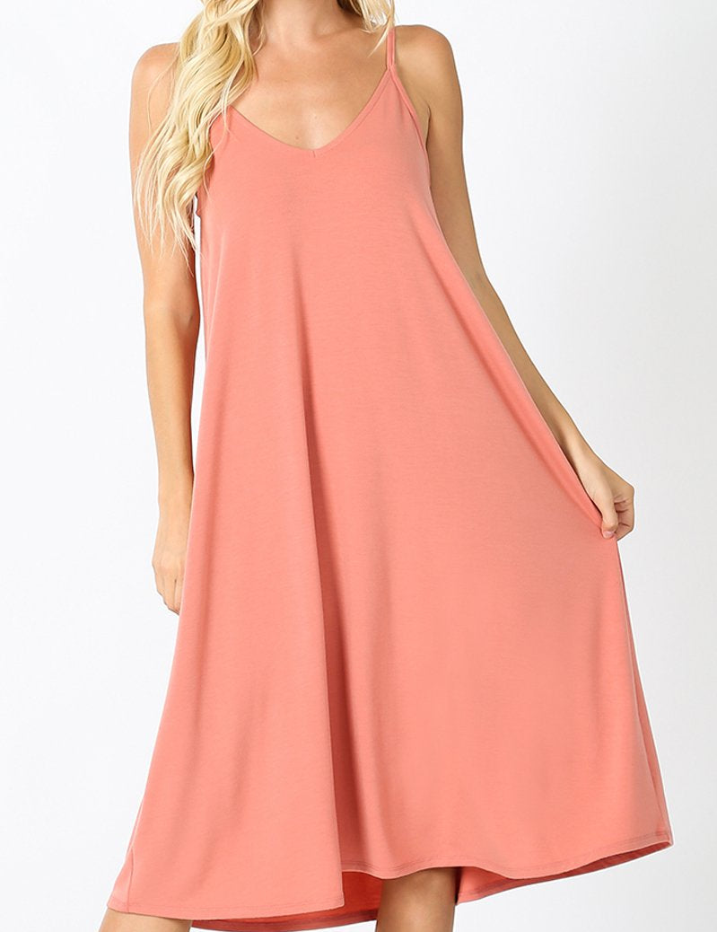 Woman wearing Maribel V-Neck Swing Dress in coral, featuring cami straps and knee-length billowy style.