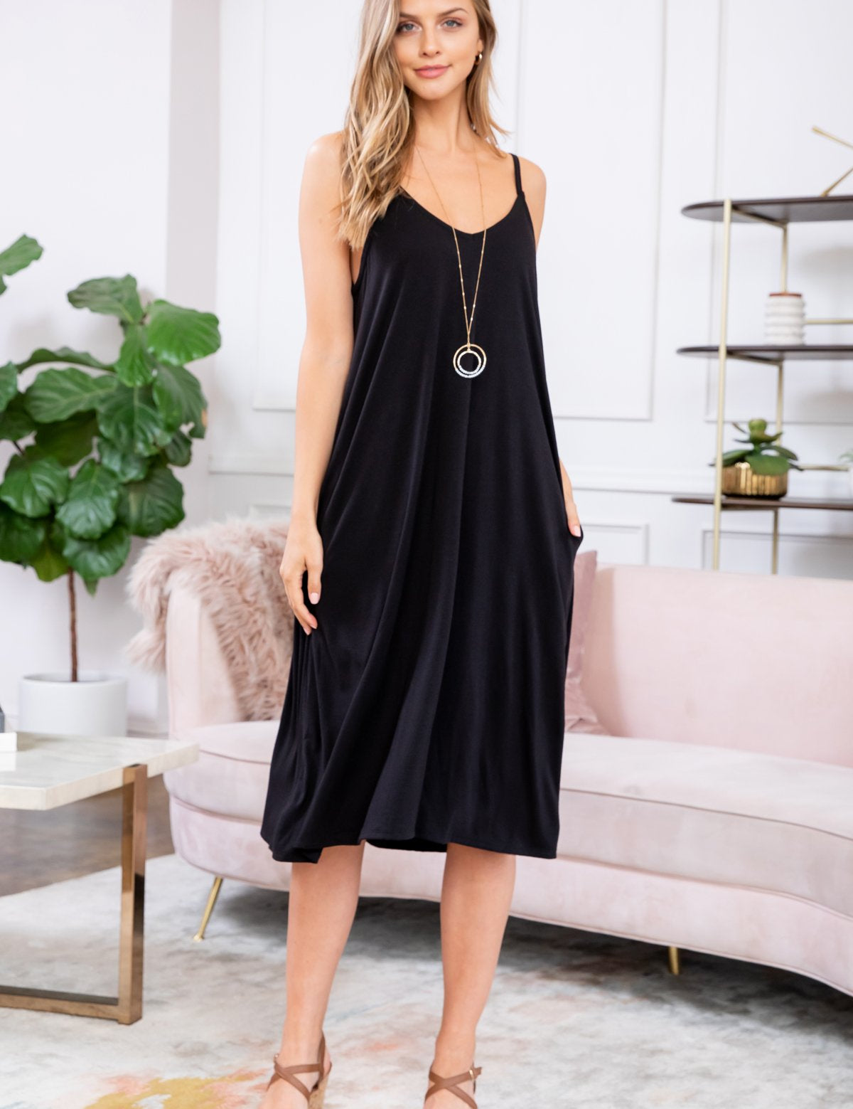 Woman wearing Maribel V-Neck Swing Dress in black with cami straps, knee-length, styled casually with sandals and a pendant necklace.