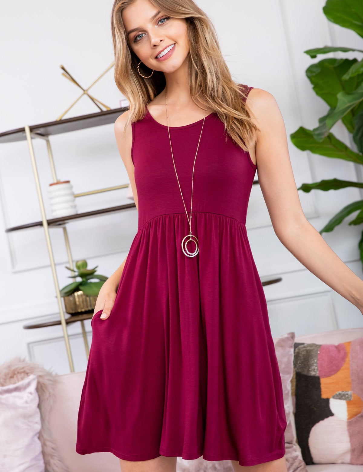 Woman wearing the Zavina Racerback Tank Dress in casual setting, featuring a flared silhouette, crew neckline, and side pockets.