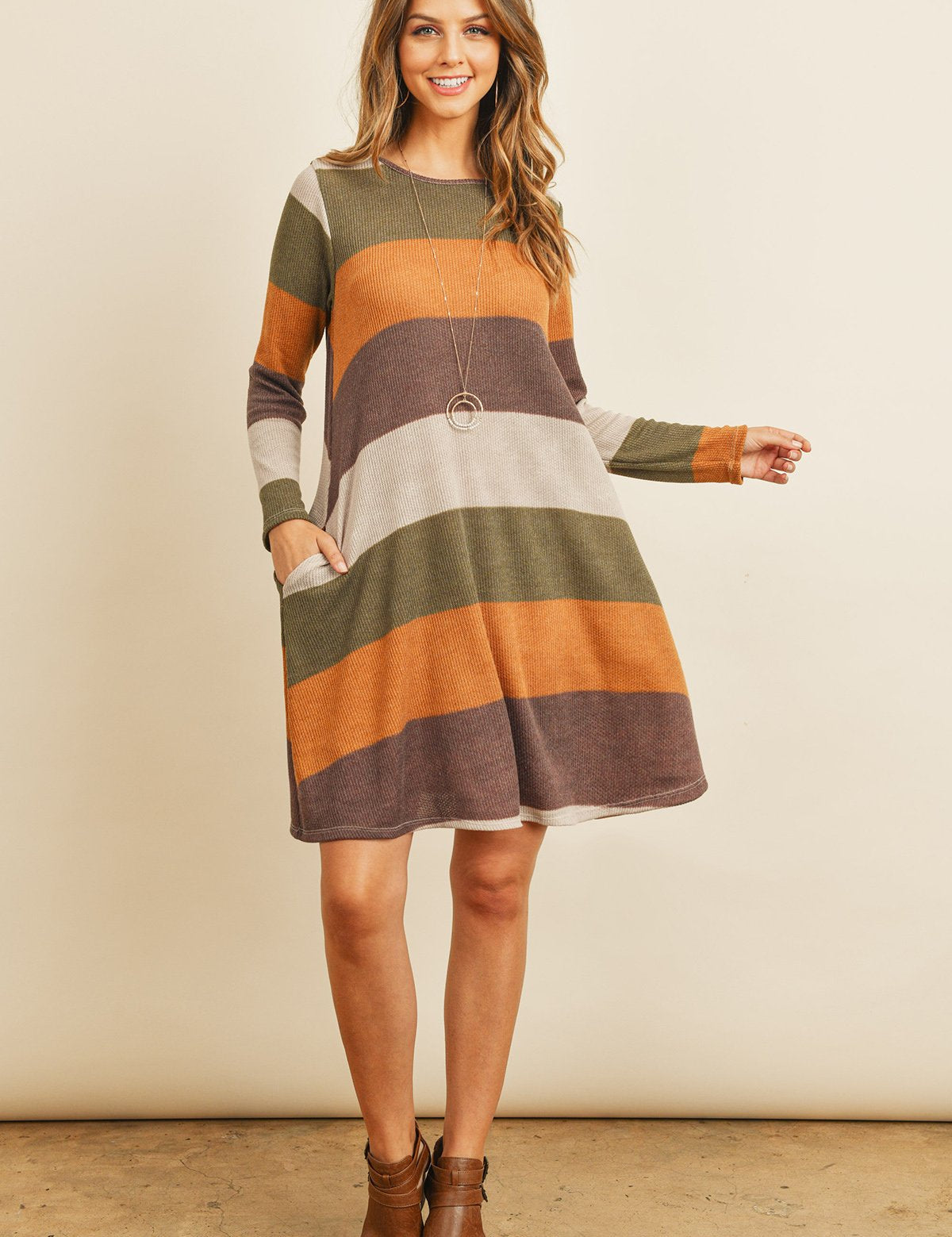 Woman wearing Solvia Ribbed Swing Pocket Dress with striped pattern, long sleeves, and side pockets, styled with ankle boots.
