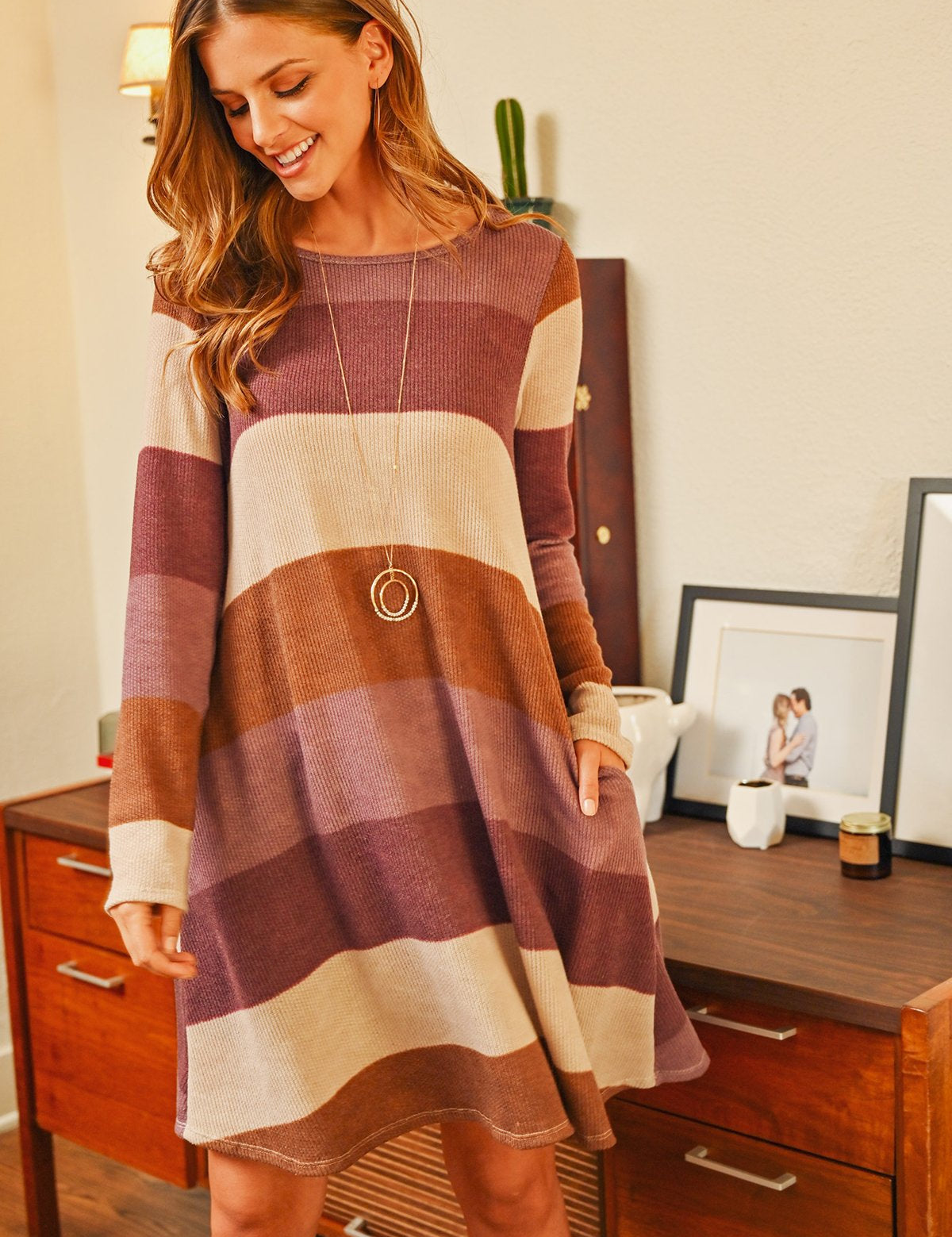 Woman wearing Solvia Ribbed Swing Pocket Dress with striped pattern, long sleeves, cozy knit texture, standing in a stylish room.