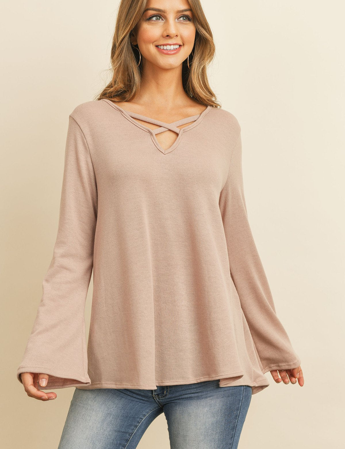 Woman wearing Evanthira Criss-Cross Knit Top with bell sleeves and criss-cross neckline, styled casually with ripped jeans.