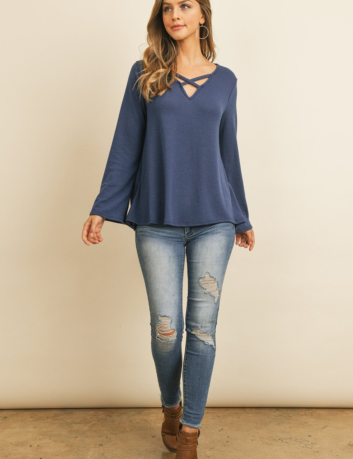 Woman wearing Evanthira Criss-Cross Knit Top with long sleeves, casual jeans, and brown boots, showcasing casual fall fashion style.